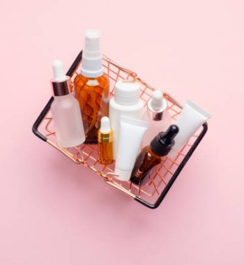 Shopping basket full of cosmetic bottles and packaging on pink background, view from above. Cosmetics sale or discount concept.